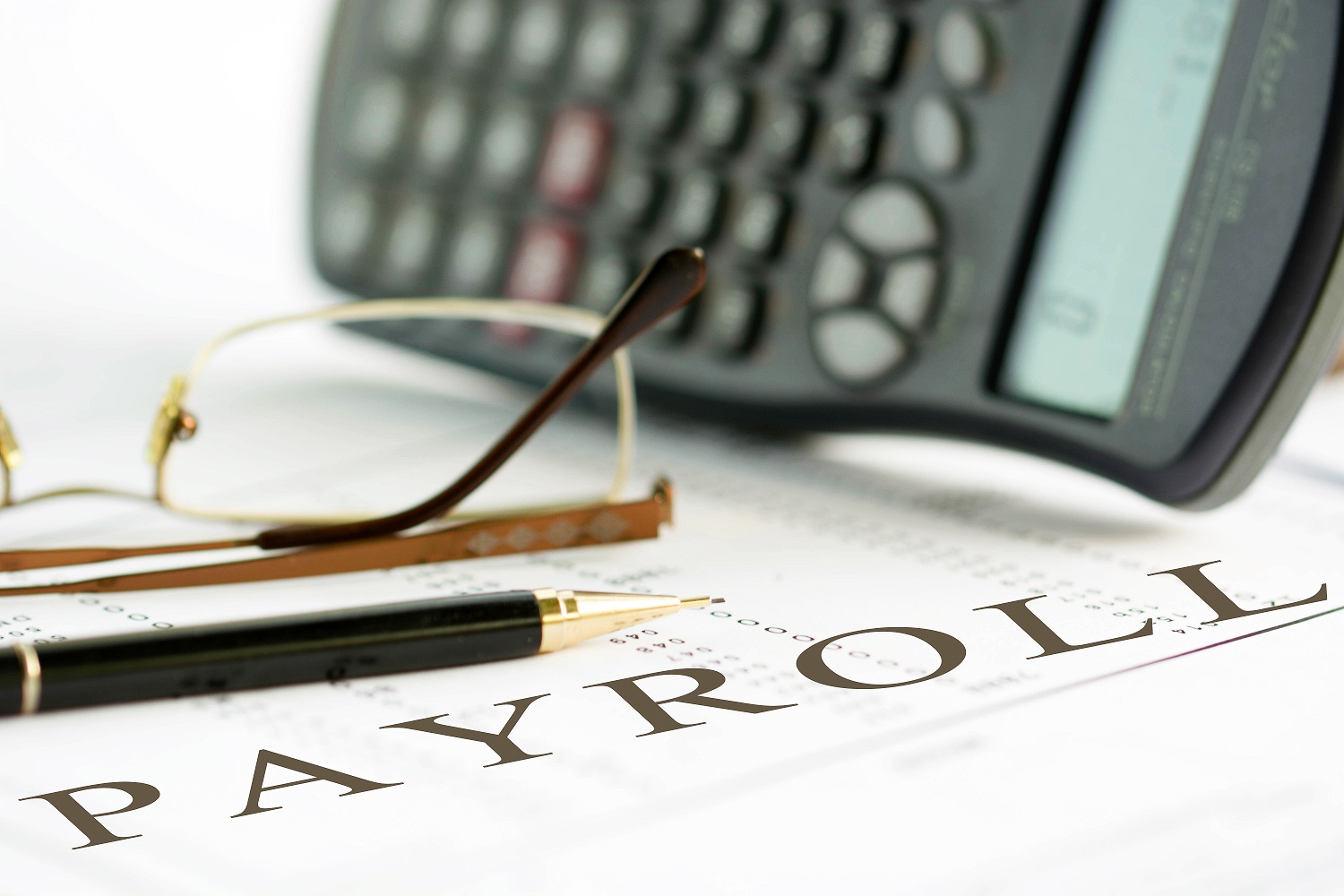 Payroll concept image of a pen, calculator and reading glasses on financial documents.